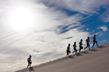 business concept success,competition,people running uphill outdoors su clouds and blue sky with group leading and one lonely runner left behind struggle to keep up 