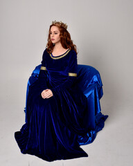 Full length portrait of  girl wearing long blue velvet gown with golden crown. sitting pose,...