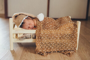 the child is lying on a wooden bed under a blanket. portrait of a small child in a warm hat with a...