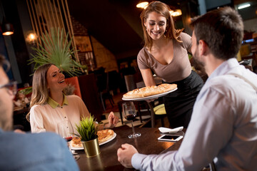 Waiter woman serving group of friends with food in the restaurant