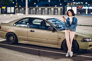 Girl stand near car and use smartphone at evening
