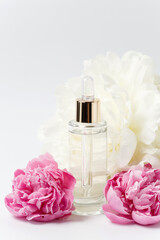 Glass transparent mockup bottle with dropper with cosmetic serum, oil, essence among pink and white peony flowers