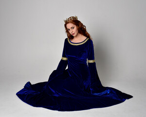 Full length portrait of  girl wearing long blue velvet gown with golden crown. sitting pose,...
