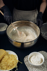 Women in checkered apron and black gloves mixing liquid yeast dough with wooden spoon. Process of making bakery. Adjarian Khachapuri Recipe – Georgian cheese bread.