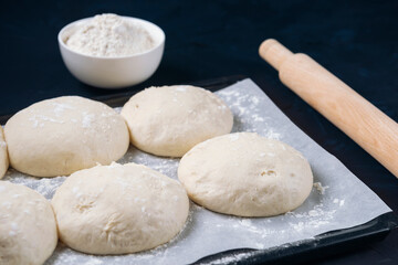A few pieces of yeast dough in baking tray with rolling pin and flour bowl. Process of making bakery. Adjarian Khachapuri Recipe – Georgian cheese bread.