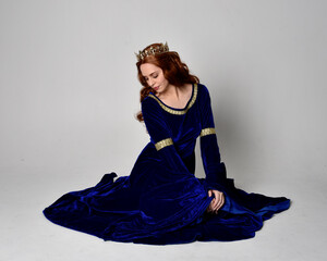 Full length portrait of  girl wearing long blue velvet gown with golden crown. sitting pose,...