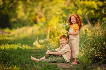 Fototapeta premium Cheerful happy Children brother and sister on a walk in the forest with a bouquet of daisies.