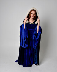 Naklejka premium Full length portrait of girl wearing long blue velvet gown with golden crown. sitting pose, isolated against a studio background.