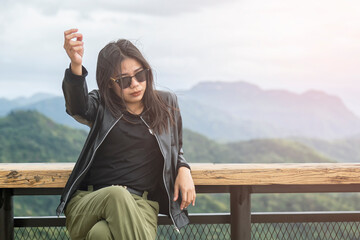 Asian woman is sitting on a wooden table waiting to watch the sunrise in the morning at rural , Thailand. Beautiful girl sitting on wooden chair with blurred green background.