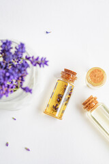 Lavender essential oil in small glass bottles and lavender flowers in a mortar, white background, top view.