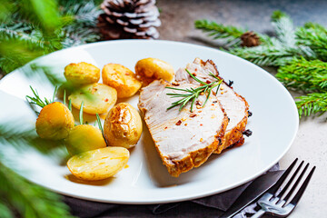 Portion of christmas baked pork loin on white plate, dark festive background. Christmas meat concept.