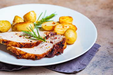 Portion of baked pork loin with potatoes on white plate, dark background.
