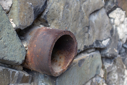 old iron drainpipe made of granite wall.