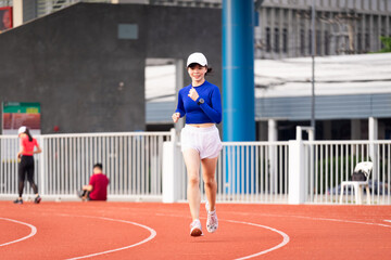 Fototapeta premium Young fitness woman runner jogging excercise in the morning on city stadium track in the city. Female athlete excercise in the city stadium to keep body fitness. Health and recreation stock photo.