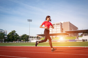 Fototapeta premium A young fitness woman runner jogging excercise in the morning on city stadium track in the city. Female athlete excercise in the city stadium to keep body fitness. Health and recreation stock photo.
