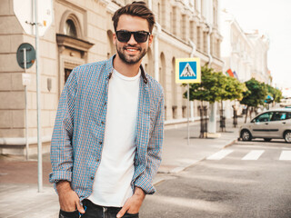 Portrait of handsome smiling stylish hipster lambersexual model.Man dressed in white T-shirt. Fashion male posing on the street background in sunglasses