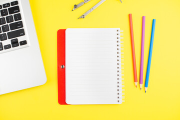 Laptop, colorful pensils, divider, and notepad planner on yellow background. Flat lay. Copy space. Workplace in the office.