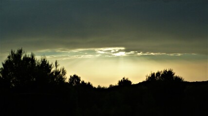 Atardecer con nubens color gris y blanca con sol sobresaliendo entre ellas
