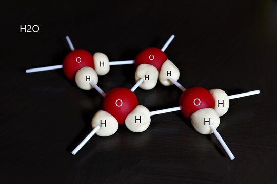 Red and White Ball and stick 3D model of the water molecule H2O on a black background.Two hydrogen atoms each share their 1 electron
with oxygen to form two covalent bonds
and make a water molecule.