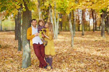 Naklejka na ściany i meble Family with daughter stand under yellow tree in park in autumn.
