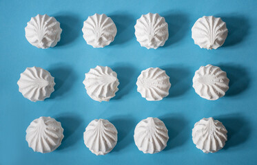 Twelve white large and delicious hand-made marshmallows lie at the same distance from each other on a blue background: a sweet background, a seamless pattern