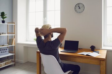 Online business. Back view of young guy with laptop having break from work, relaxing in home...
