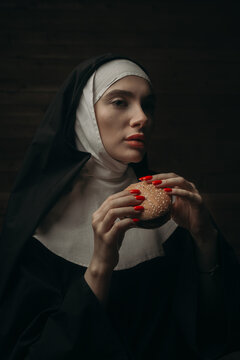 
Attractive nun eating burger with indifferent expression on her face. Holding a hamburger