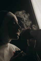 beautiful girl nun smokes an electronic device and looks into a smartphone
