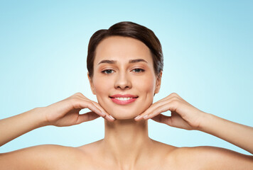 beauty, bodycare and people concept - beautiful young woman touching her face and chin over blue background