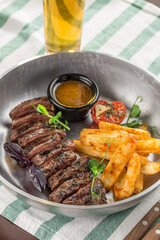 Sliced medium rare grilled Steak Ribeye with french fries and glass of beer on the table