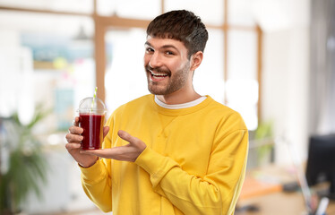drinks and people concept - happy smiling young man holding tomato juice in takeaway plastic cup with paper straw over office background