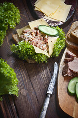 closeup of tuna fish sandwich with green salad, cheese slices, fresh cucumbers and bread, on dark wooden table background