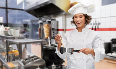 cooking, culinary and people concept - happy smiling female chef in toque with saucepan over restaurant or kebab shop kitchen background