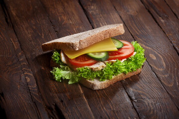 turkey sandwich closeup with fresh tomatoes, lettuce salad leaves, cucumber and cheese, on wooden rustic table background