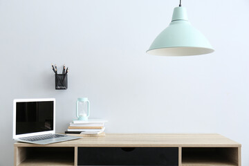 Stationery with laptop and hourglass at workplace near light wall