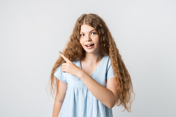 Fototapeta premium You better see it! Intrigued European girl with curly long hair, points away with one finger, shows blank space for your promotion. People, advertisement concept