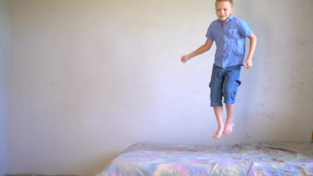 one boy in shorts and T-shirts are jumping on bed. Child love to play. Simple sports exercises at home