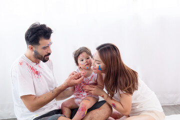 Obraz na płótnie Canvas Happy mixed race family and half-Turkish baby girl playing fun together paint face and paper, father, mother, parenthood hug adorable daughter paint color on dirty white clothes, hands and face