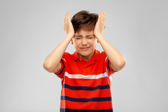 childhood, fashion and people concept - portrait of stressed boy in red polo t-shirt having headache over grey background