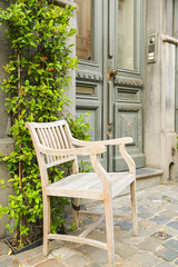 An old white wooden chair in front of a vintage door and a wall full of green plants