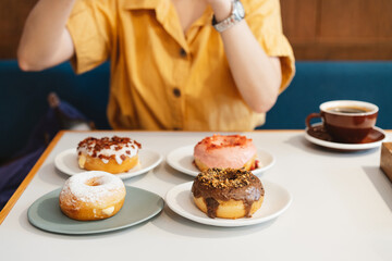 Woman wearing yellow shirt taking photos of strawberry pink, chocolate, sugar glazed and bacon cheese donut with feeling happy a modern cafe. Enjoyment female lifestyle.