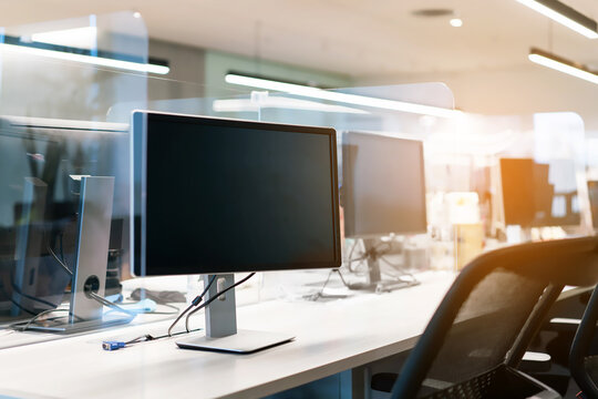 Acrylic plexiglass separator setting on the desk with monitor in the office. New normal Concept for social distancing in offices during the Covid-19 pandemic. Precaution and safe.