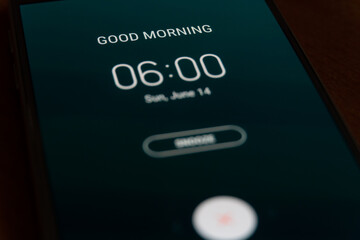 On a black smartphone, an alarm clock rings for 6 am with the inscription Good morning close-up,...