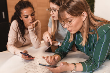 Group of modern young business women in casual wear discussing architectural designs in the creative office.