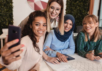 Group of modern young business women in casual wear discussing architectural designs in the creative office.
