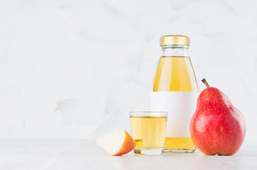 Fresh yellow transperent pear juice in glass bottle mock up with blank label,  wine glass, fruit slice on white wood table in light interior, template for packaging, advertising, design.