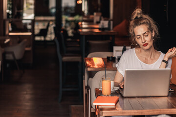 Smiling senior female blogger in casual wear sitting in cafe using laptop and smartphone.