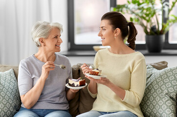 family, generation and people concept - happy smiling senior mother and adult daughter eating cake at home