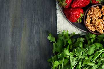 container with healthy strawberries with walnuts, seed omelette and green plants, grouped on the right on a white cloth on a dark table