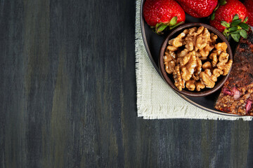 container with healthy strawberries, nuts and seed omelet, grouped on the right on a white cloth on a dark table